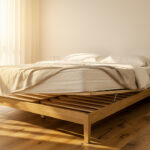 Chambre lumineuse de style éditorial avec un lit double, un matelas blanc et un sommier à lattes en bois apparent.