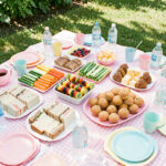 Goûter anniversaire pique-nique enfants : menu sûr Goûter d’anniversaire en plein air avec un menu varié et adapté aux enfants, présenté sur une nappe de pique-nique colorée.
